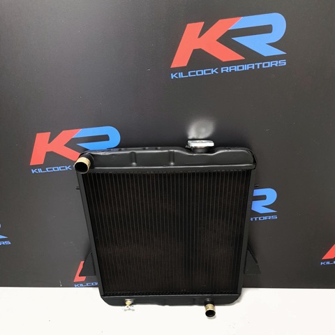 A black-finished radiator with brass inlet and outlet, in front of the red and blue KR backdrop